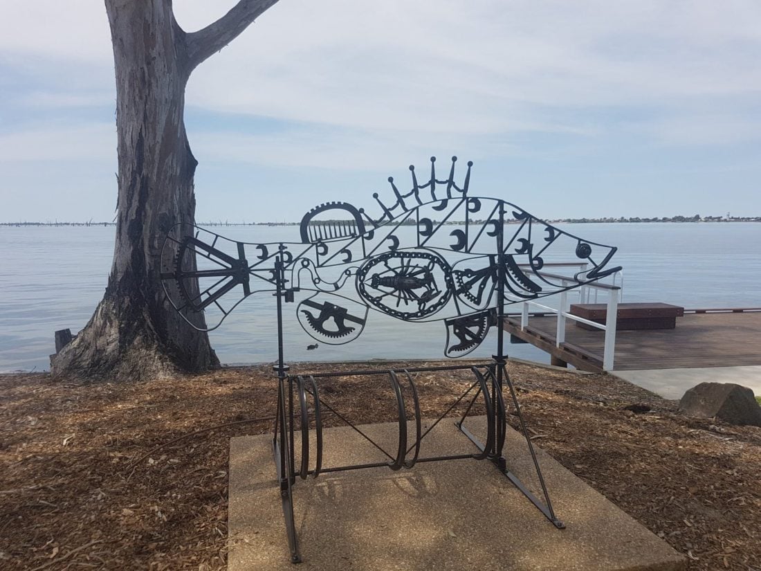 A scrap metal sculpture of a fish is silhouetted against Lake Mulwala.