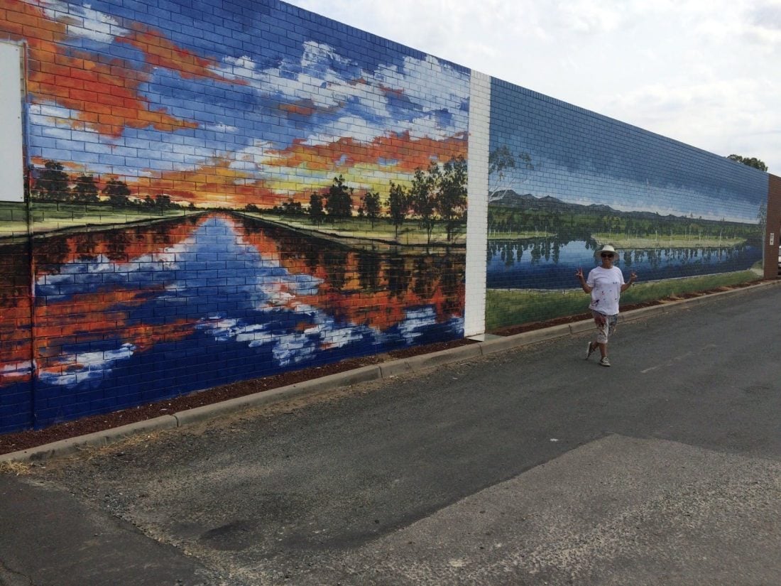 Two murals of the Murray River on a brick wall in Howlong. One is a sunset; the other is blue sky.